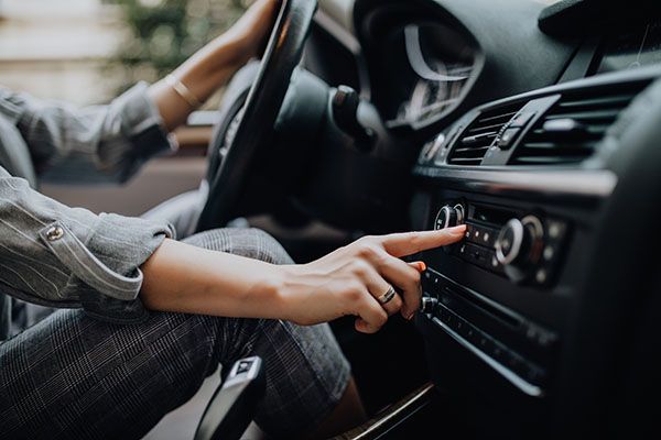 Person in car, hand on dashboard adjusting radio. | Dave's Automotive LLC