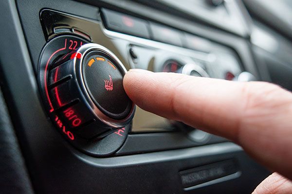 Hand turning a car's temperature control dial, which is illuminated in red. | Dave's Automotive LLC