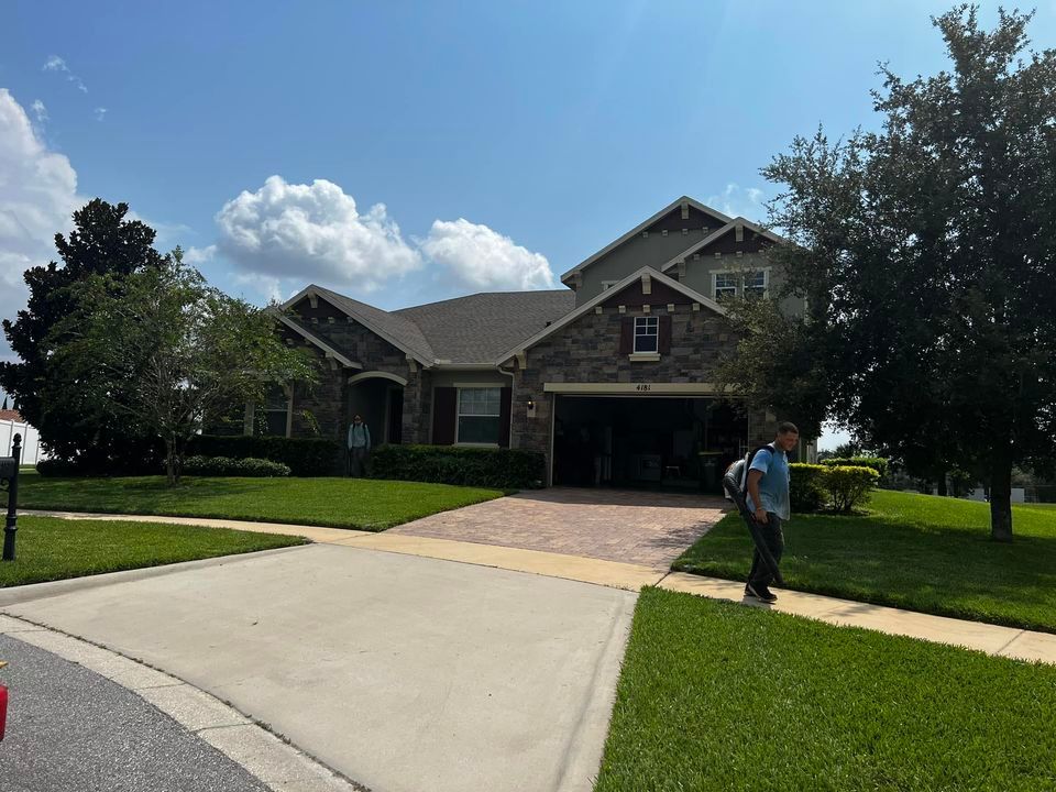 Two-story house with green lawn, blue sky, and a person standing by the driveway.