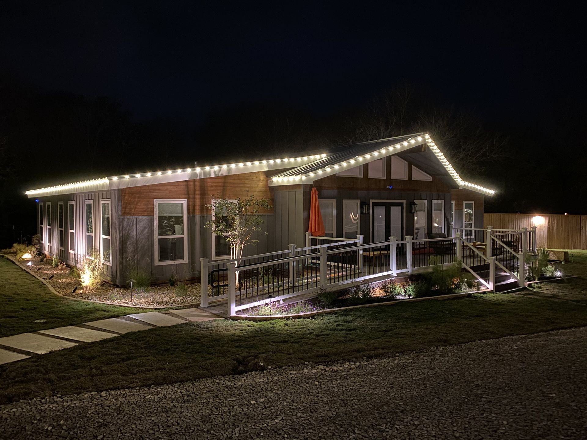 House exterior illuminated with white lights at night; a ramp and walkway.