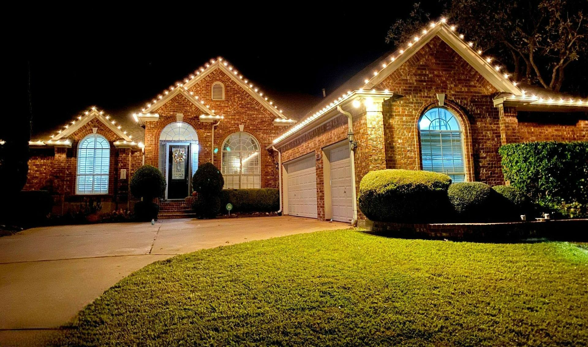 House with Christmas lights on roof and trim, lit up at night.