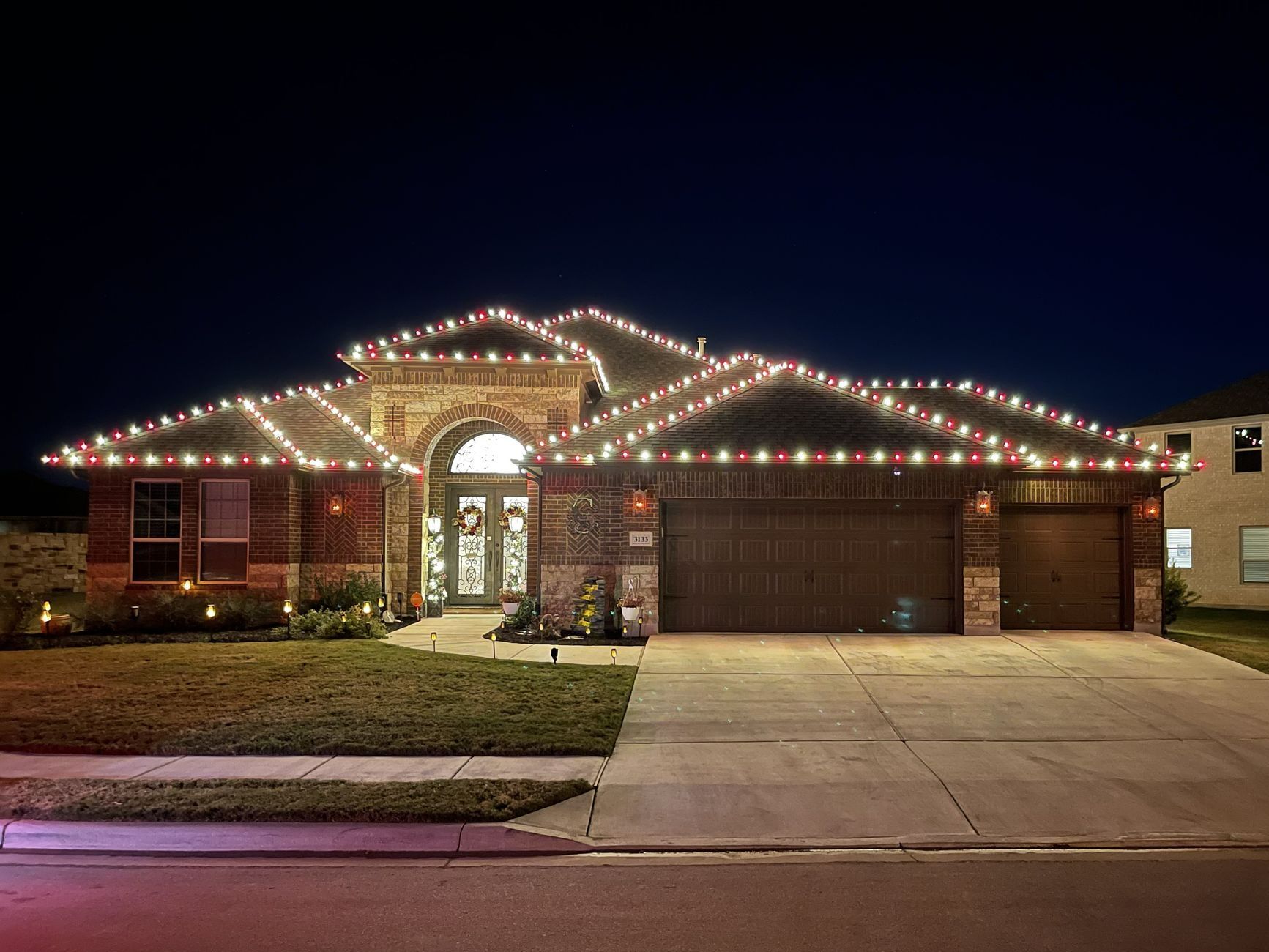 A house decorated with red and white Christmas lights along the roof against a dark night sky.