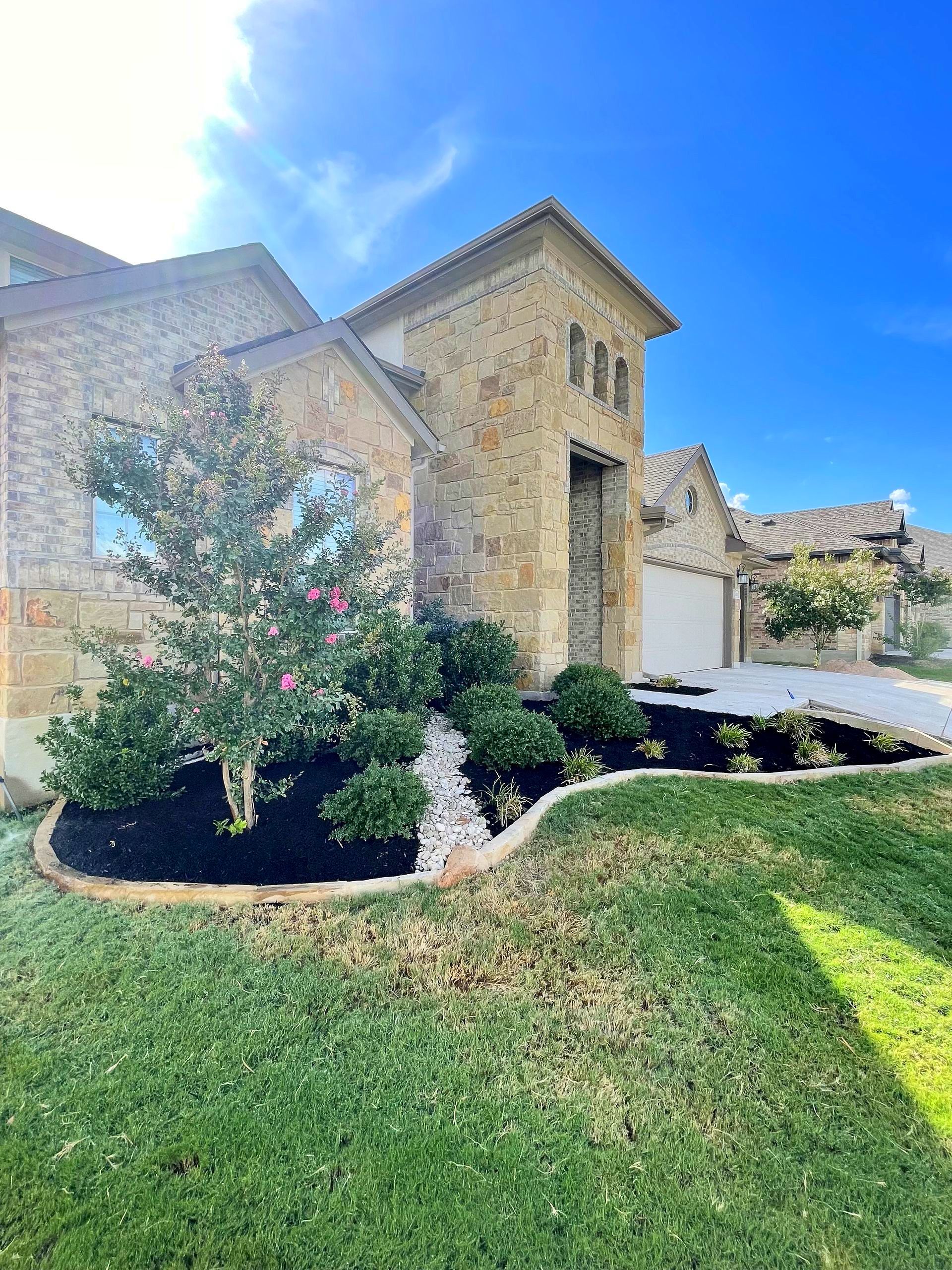 Stone house with manicured lawn, black mulch, and white rock landscaping.