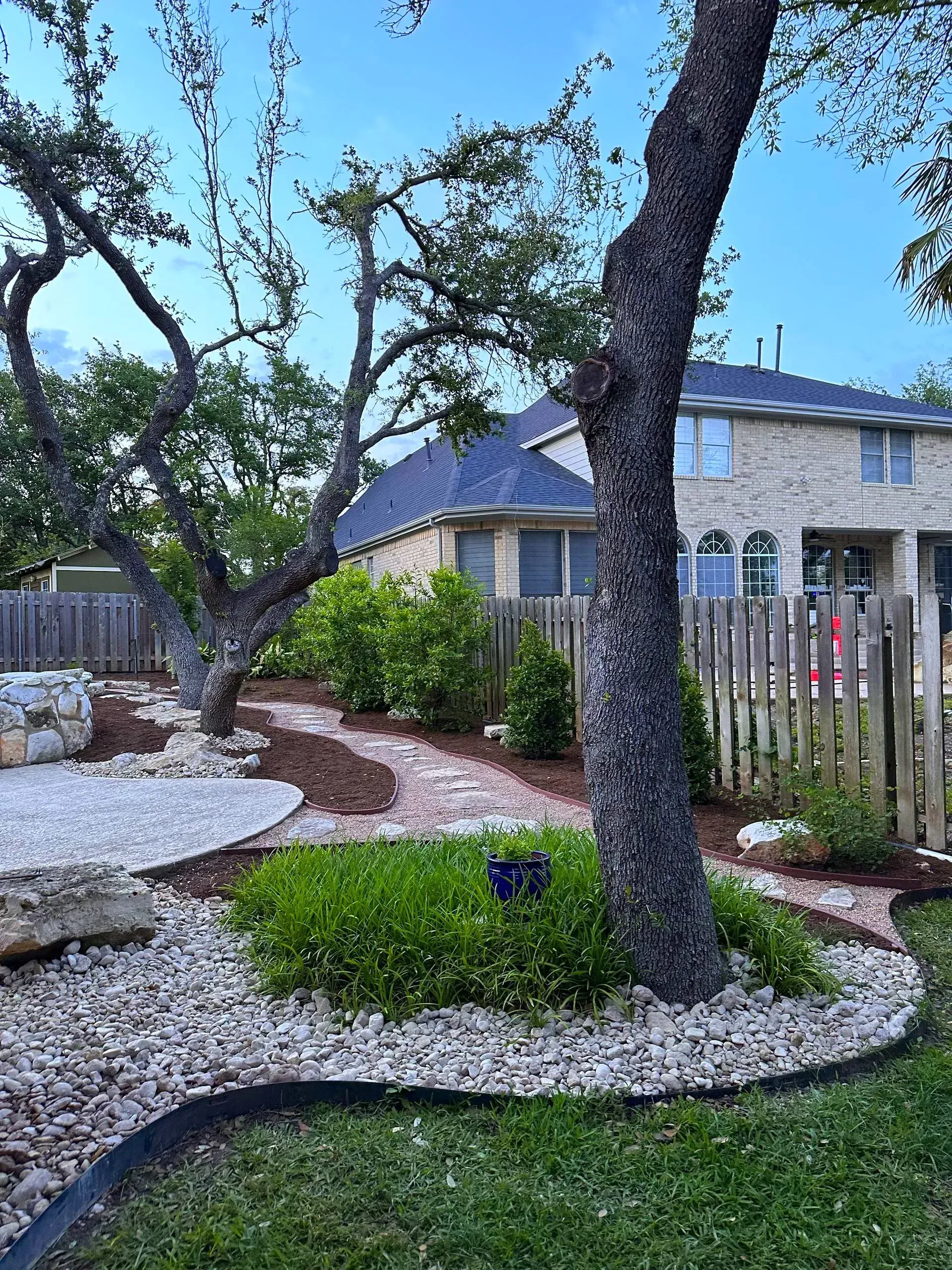 Landscaped backyard with trees, stone, mulch path, and two-story house.