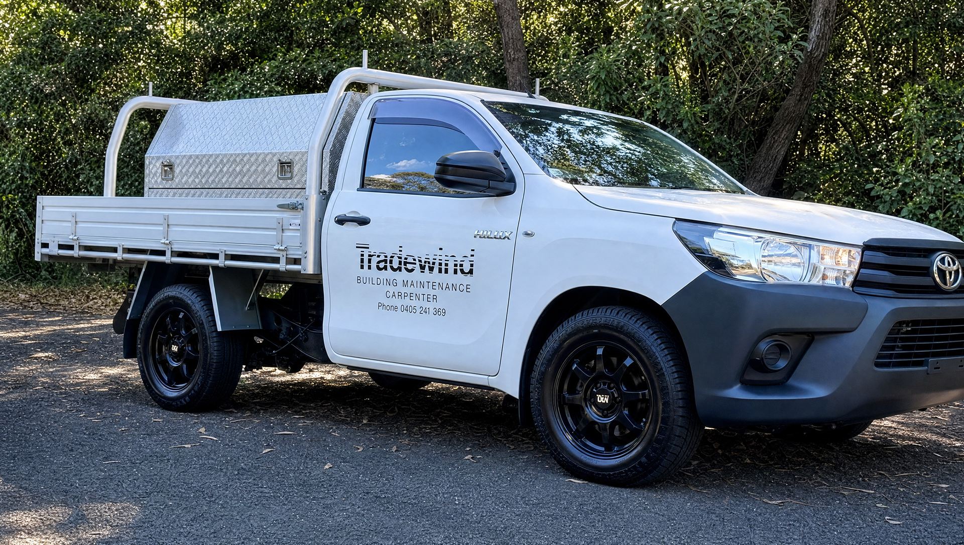 White utility truck with tray bed parked on a gravel road beside trees