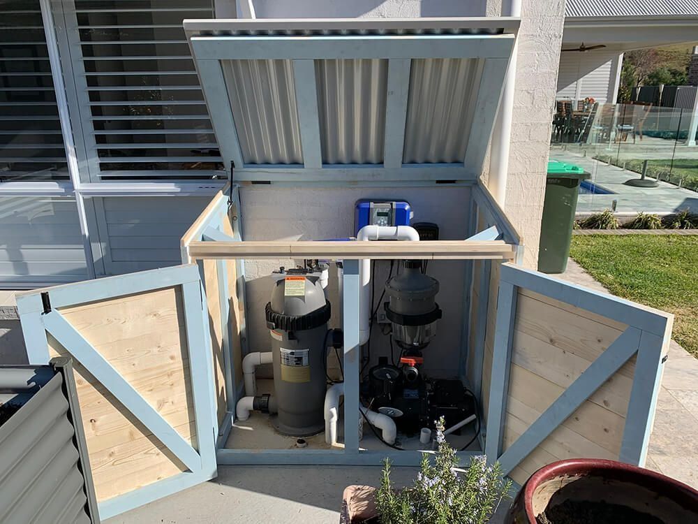 Open outdoor pool equipment cabinet with filter and pump units beside a house