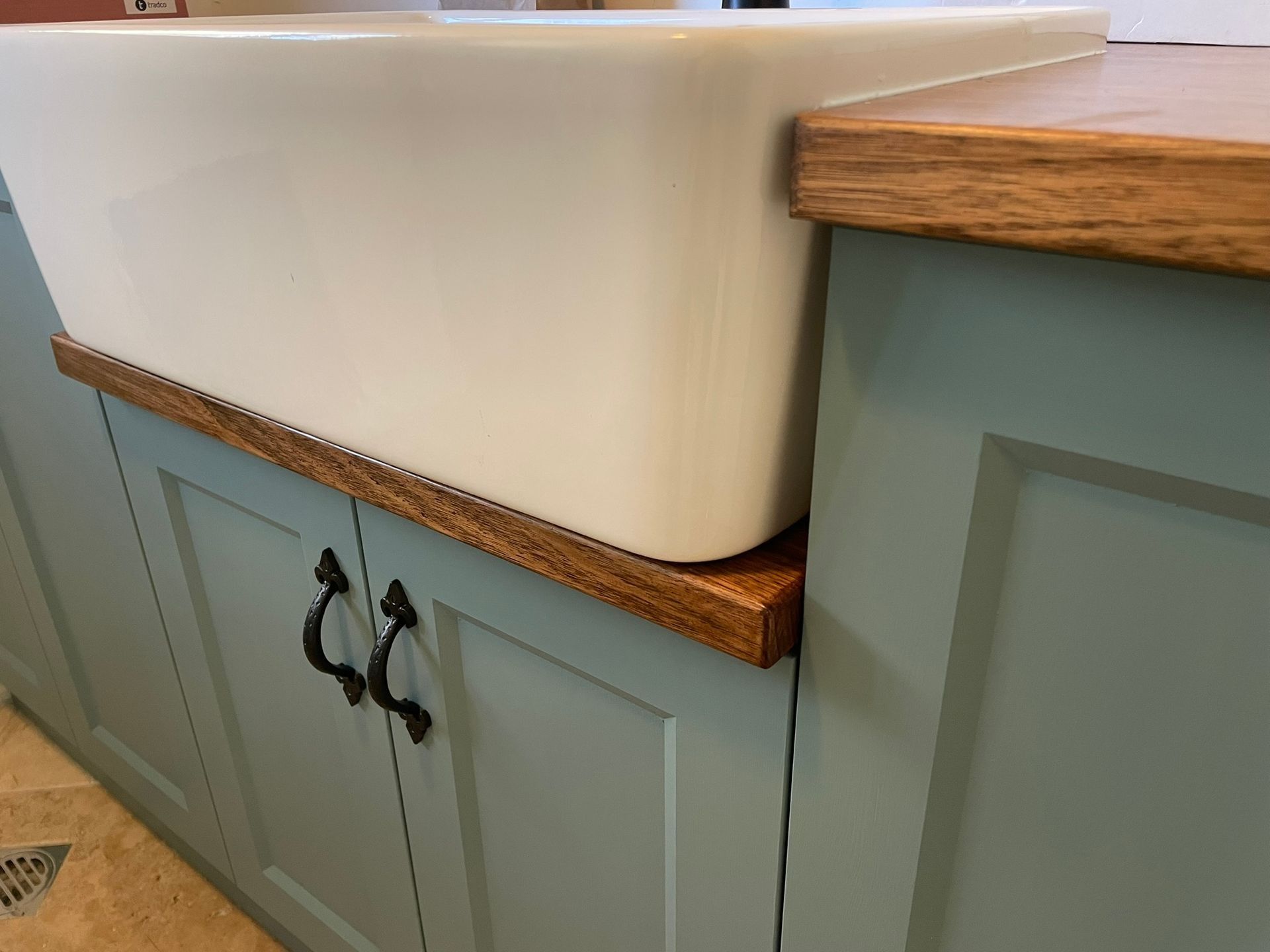 White farmhouse sink on a teal cabinet with wooden countertop trim