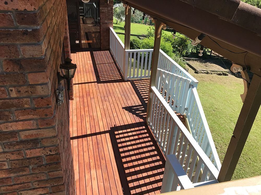 Covered wooden porch with white railing and brick wall, overlooking a green yard