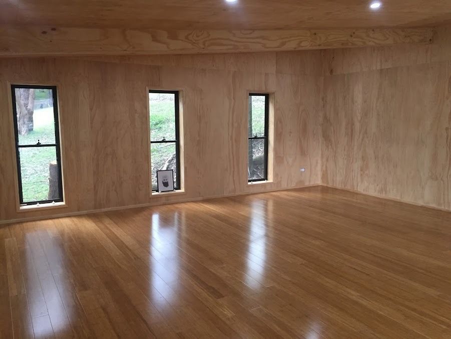 Empty wood-paneled room with polished hardwood floor and three narrow windows.