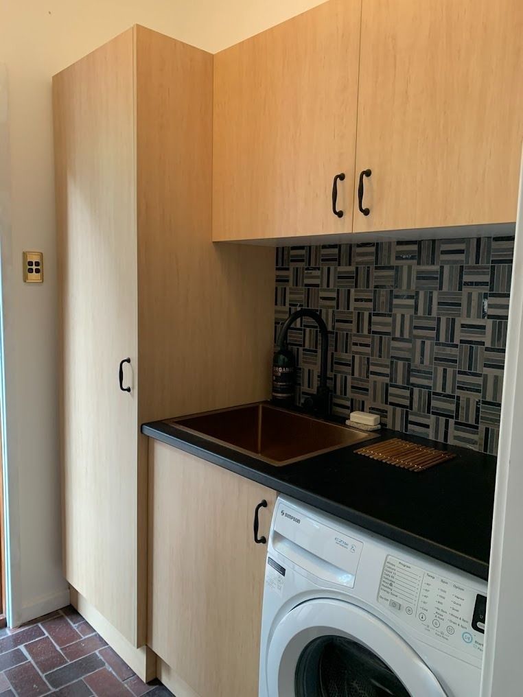 Small kitchen nook with wooden cabinets, sink, black countertop, and a washing machine under the counter