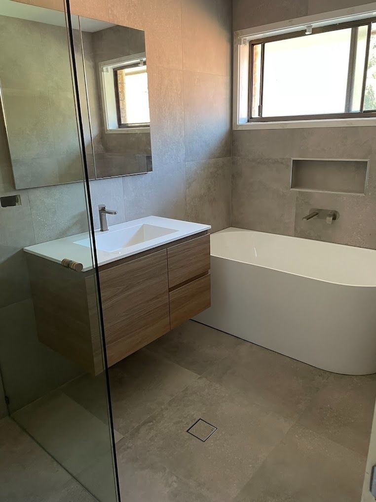 Modern bathroom with floating vanity, glass shower, and freestanding tub under windows