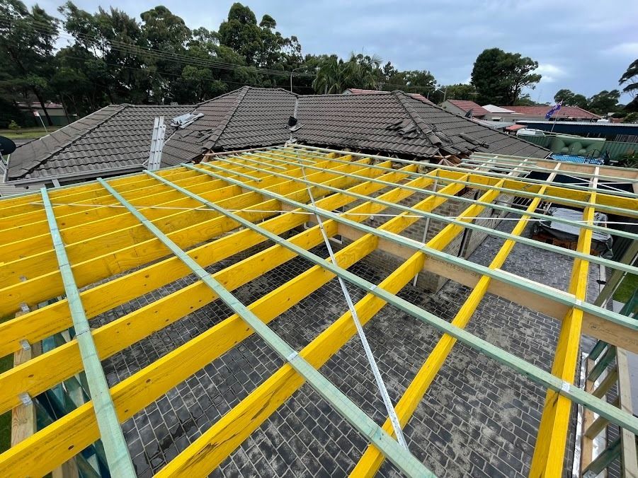 Roof under renovation with bright yellow and green support beams and damaged tiles under a cloudy sky