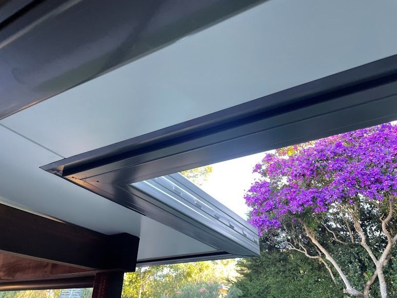 Partially open skylight with blue sky and purple flowering tree visible outside