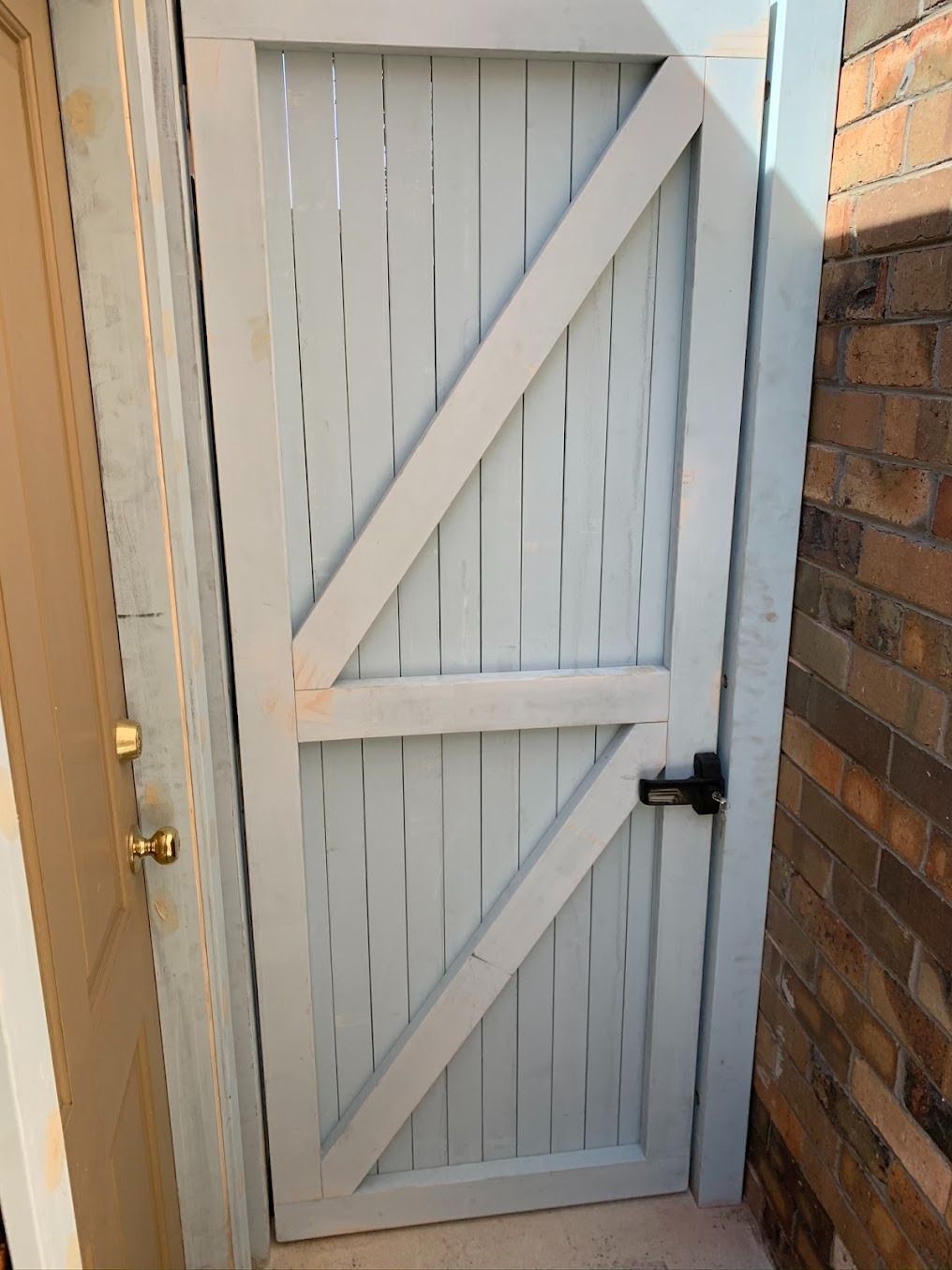 White wooden gate with diagonal braces between brick walls, closed.