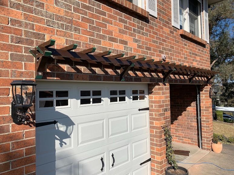 Brick house garage with a white door and a wooden pergola awning above it