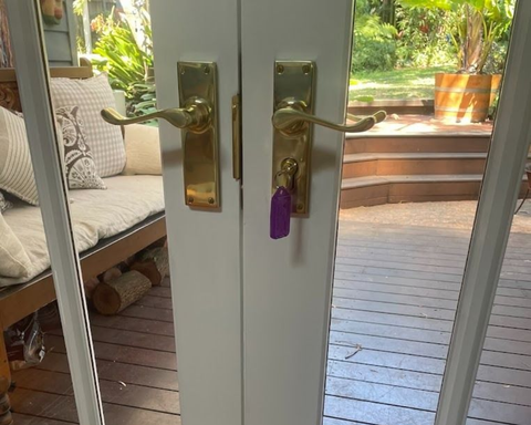 White French doors with brass handles, one secured with a purple lock, opening to a wooden deck and patio.