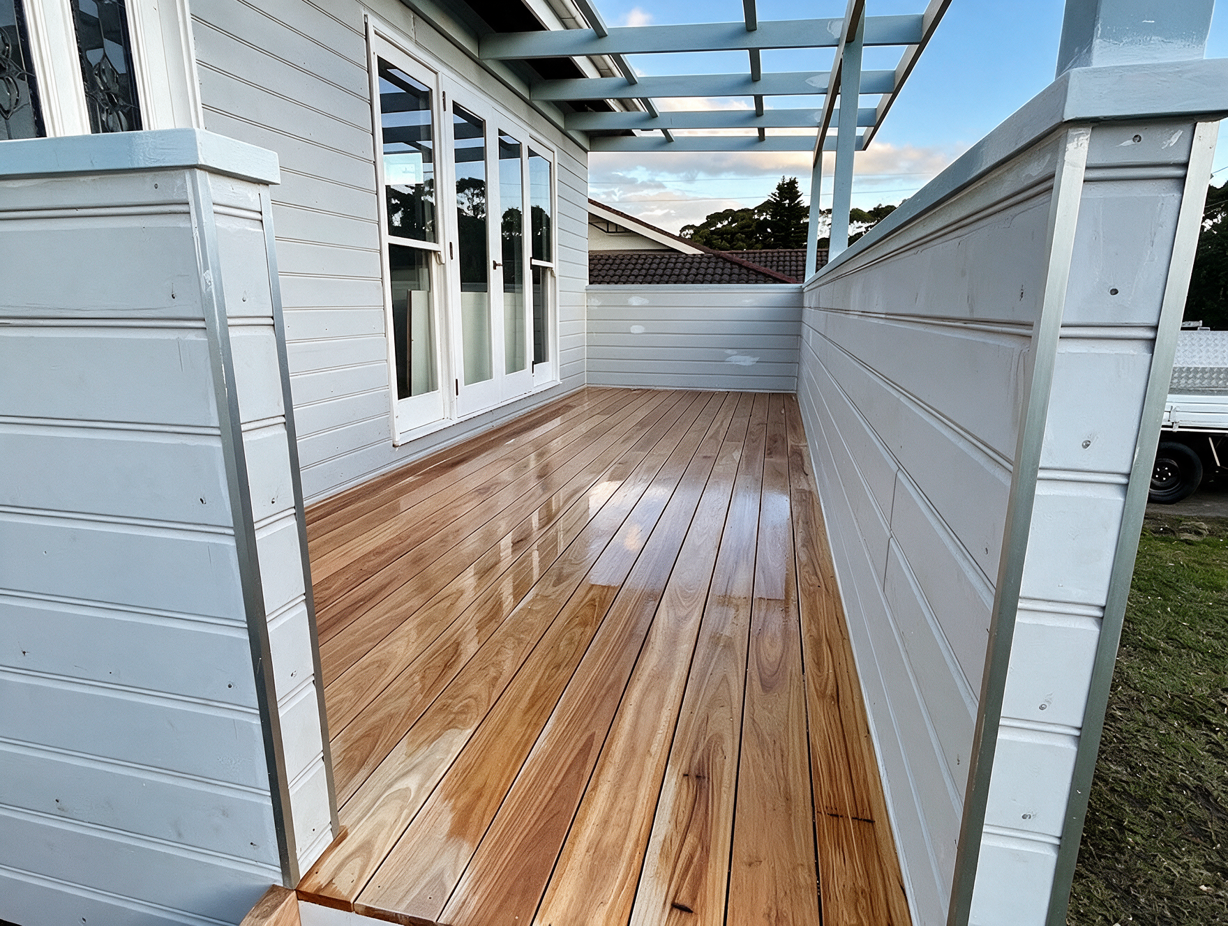 Wooden deck walkway between light gray fences and house windows, leading to a small enclosed patio area.