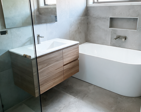 Modern bathroom with a white tub, floating wood vanity, and gray tiled walls.
