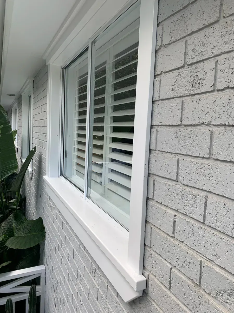 White shuttered window on a light gray brick exterior wall beside a narrow porch