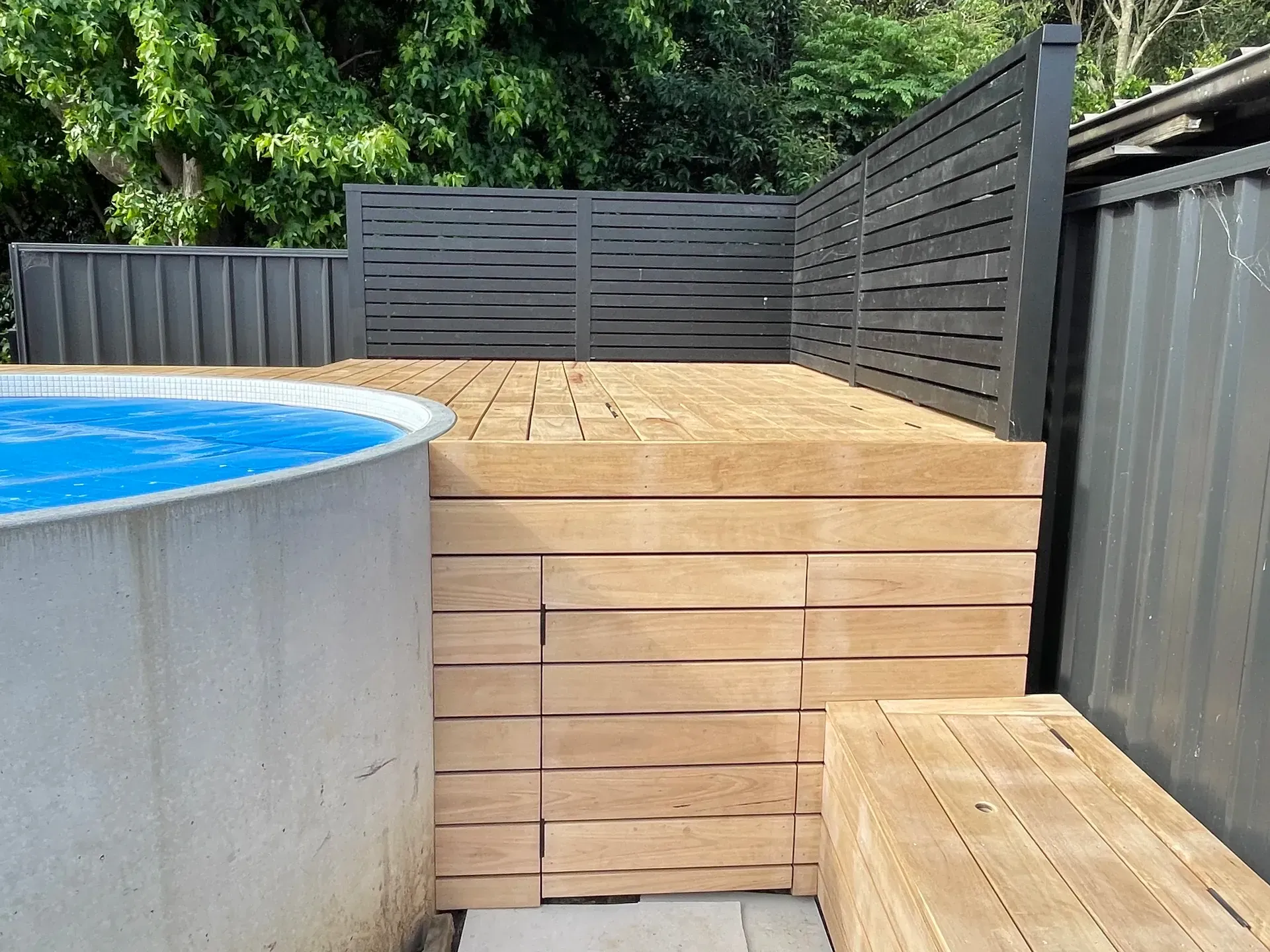 Wooden deck and steps beside an above-ground pool, with dark privacy fencing