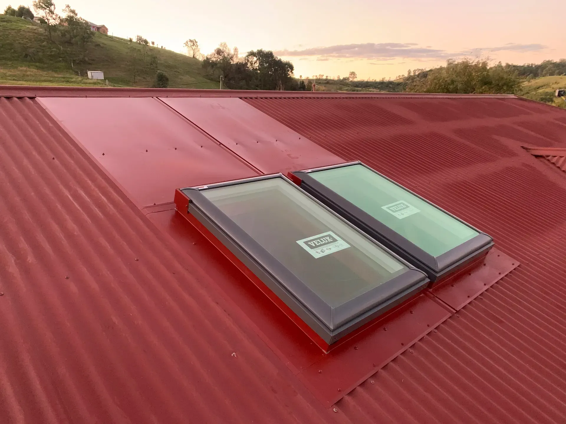 Two skylights on a red corrugated metal roof at sunset.