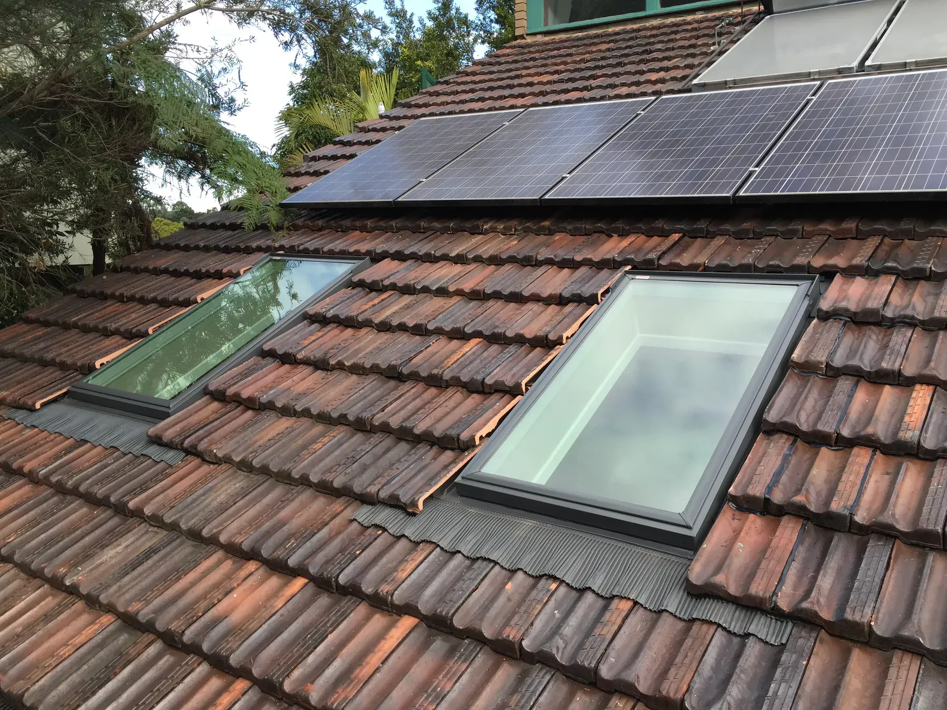 Slate-tiled roof with solar panels and two skylight windows in a wooded setting