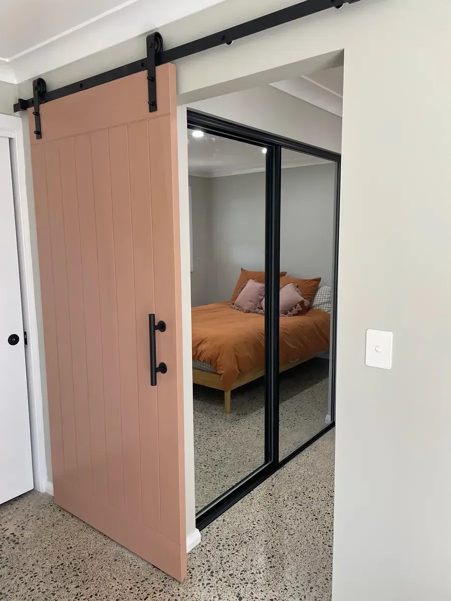 Sliding barn door partially open to a bedroom with mirrored closet doors and an orange bedspread