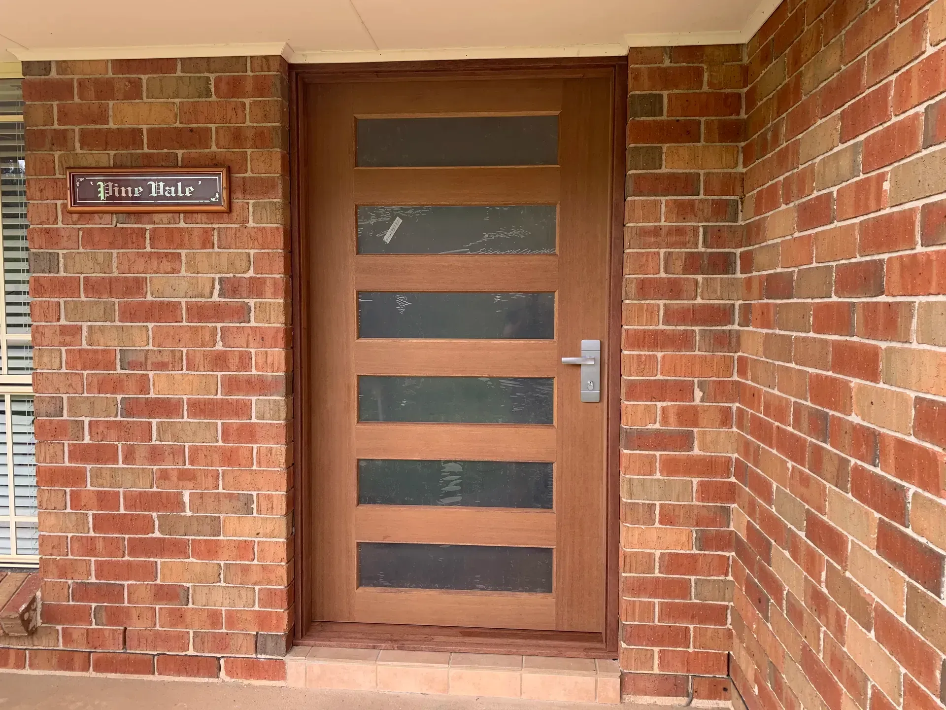 Brick house entrance with a wooden front door and a small wall plaque.