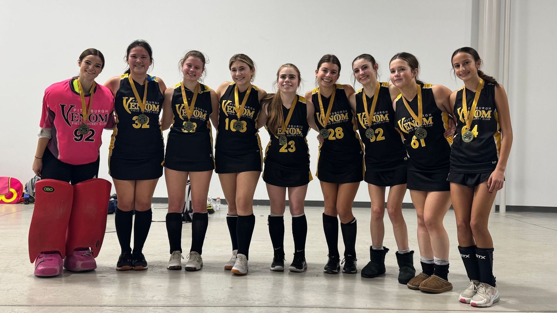 Field hockey team in black and gold uniforms with medals, posing together.