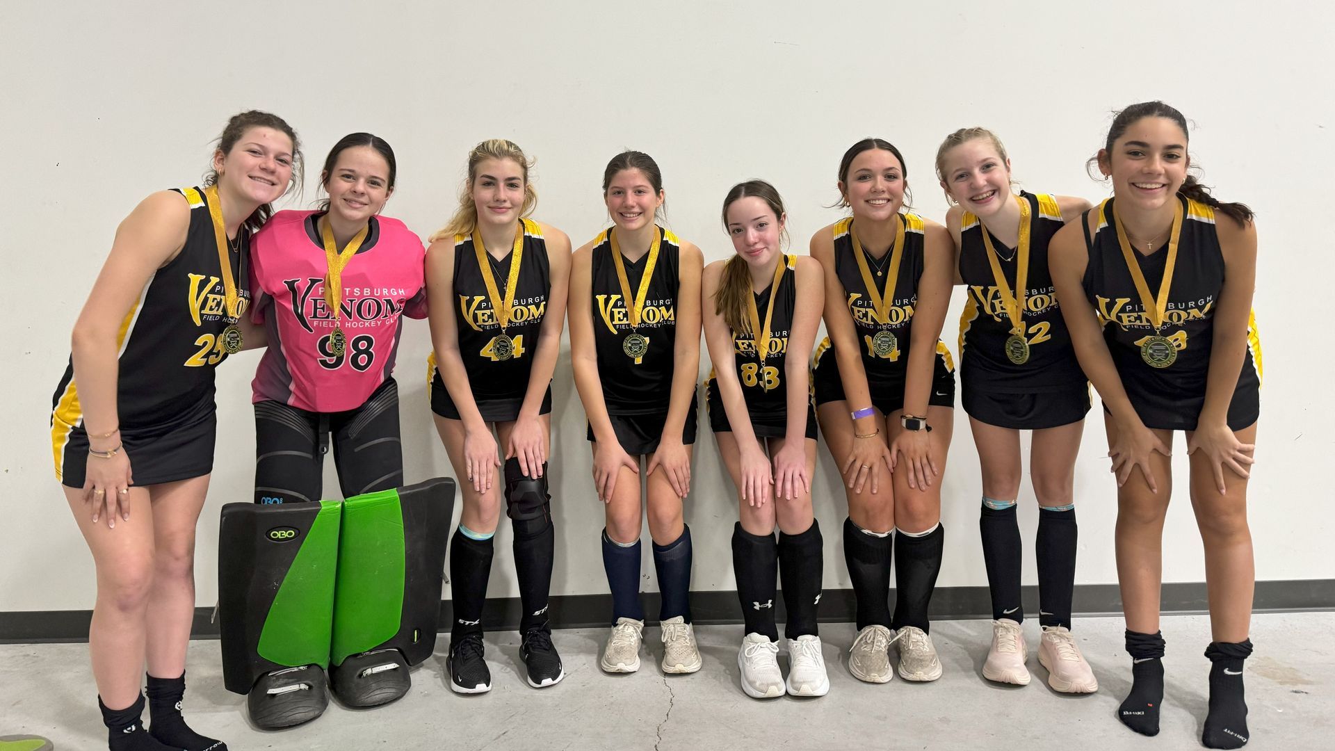Field hockey team in black and gold uniforms with medals posing in front of a wall.