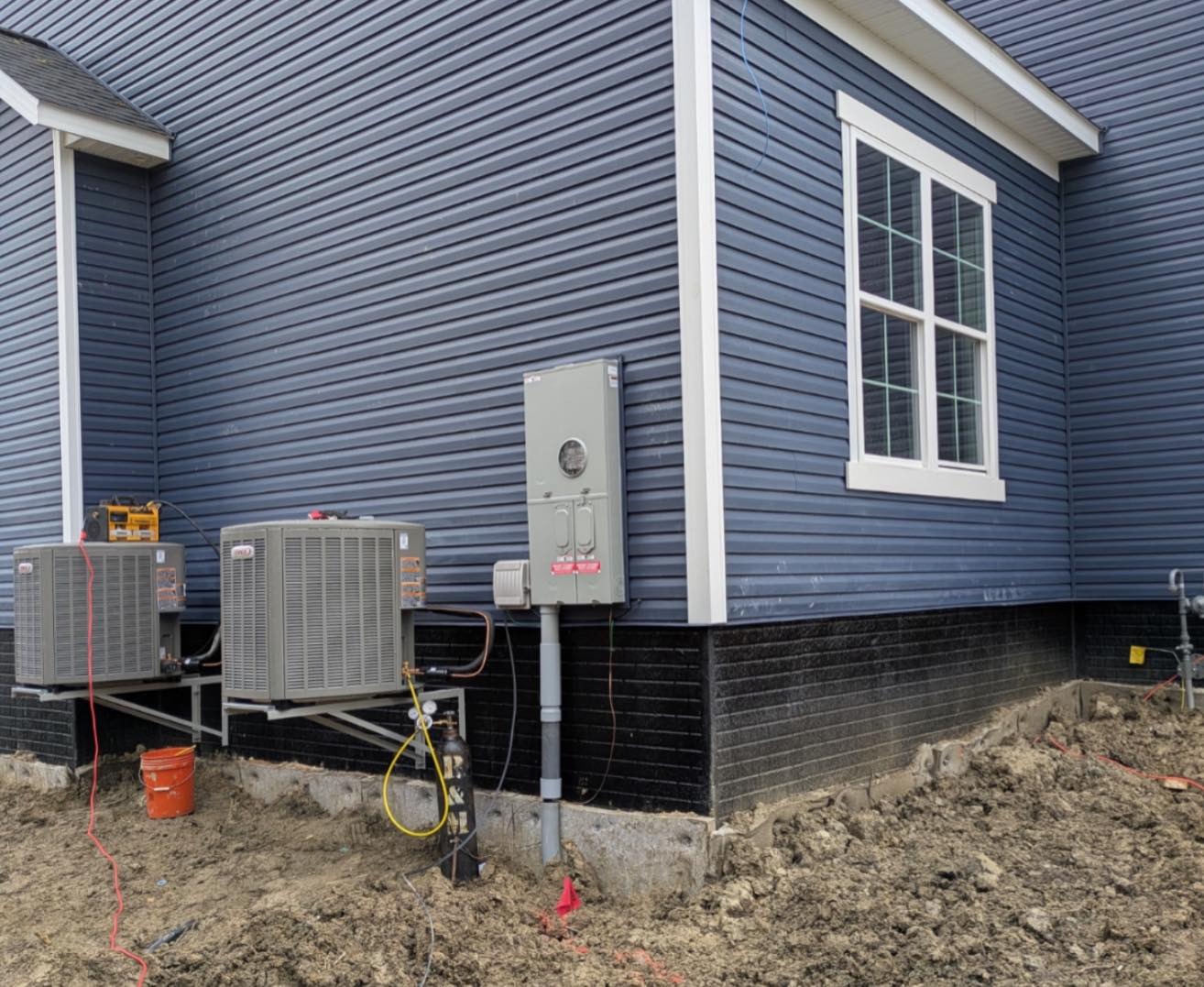 Blue house exterior with installed HVAC units and exposed wiring on muddy ground