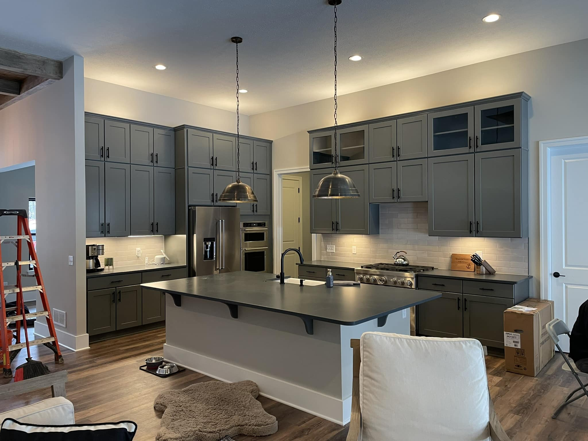Modern kitchen with gray cabinets, large island, pendant lights, and stainless steel appliances