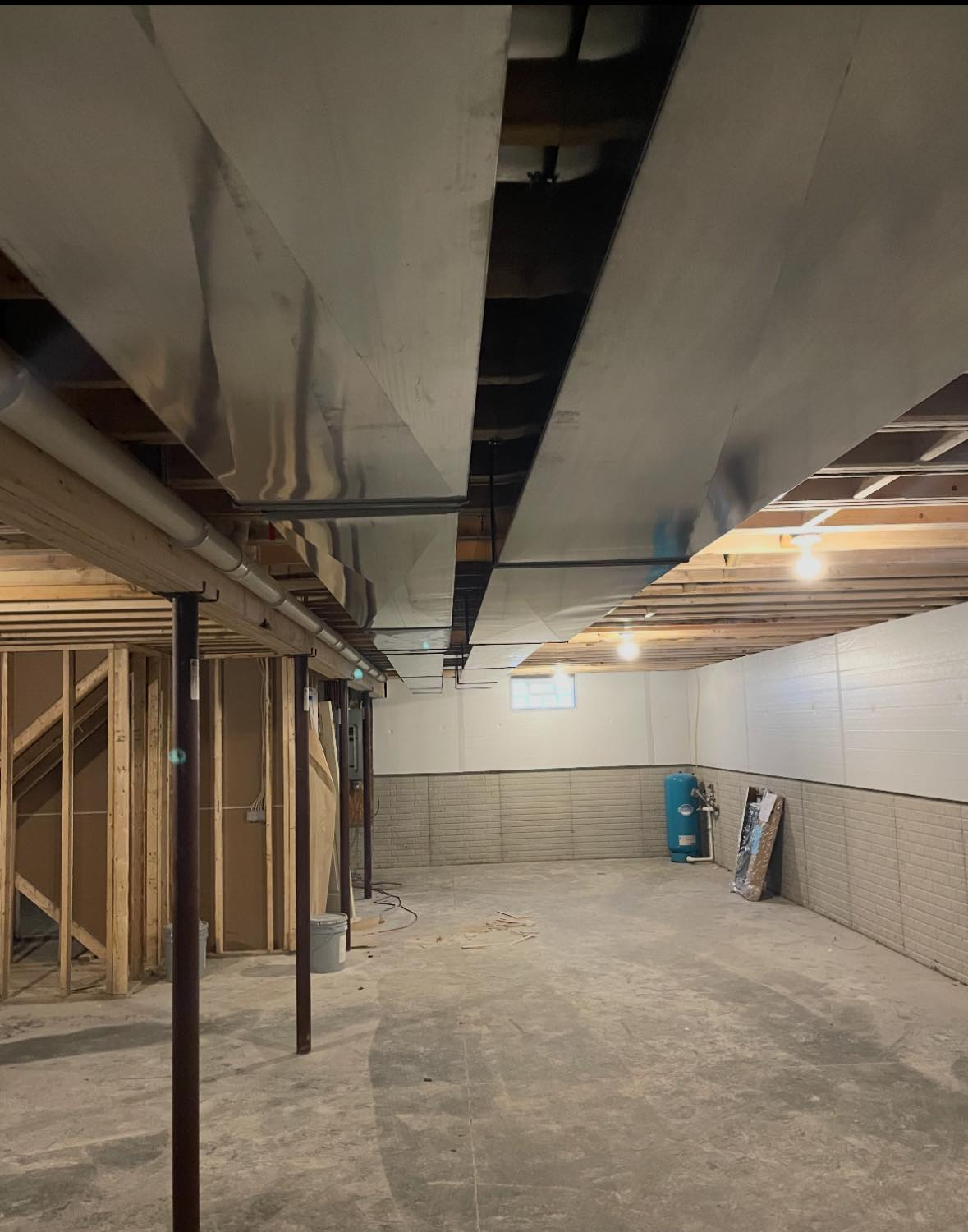 Unfinished basement interior with exposed ceiling beams, concrete floor, and construction materials along the walls.