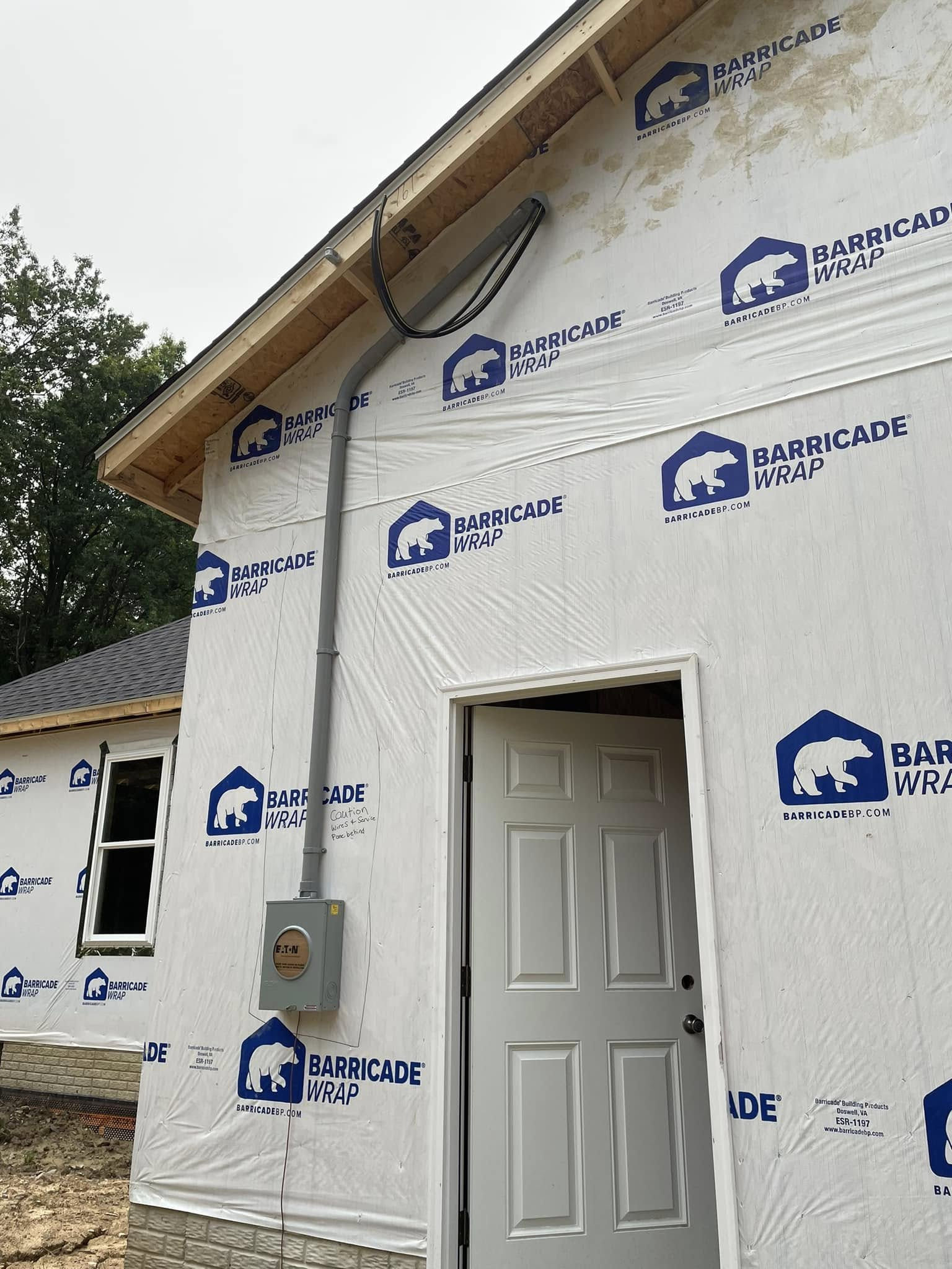 Partially finished house wrapped in white weather barrier with blue logos and an open front door