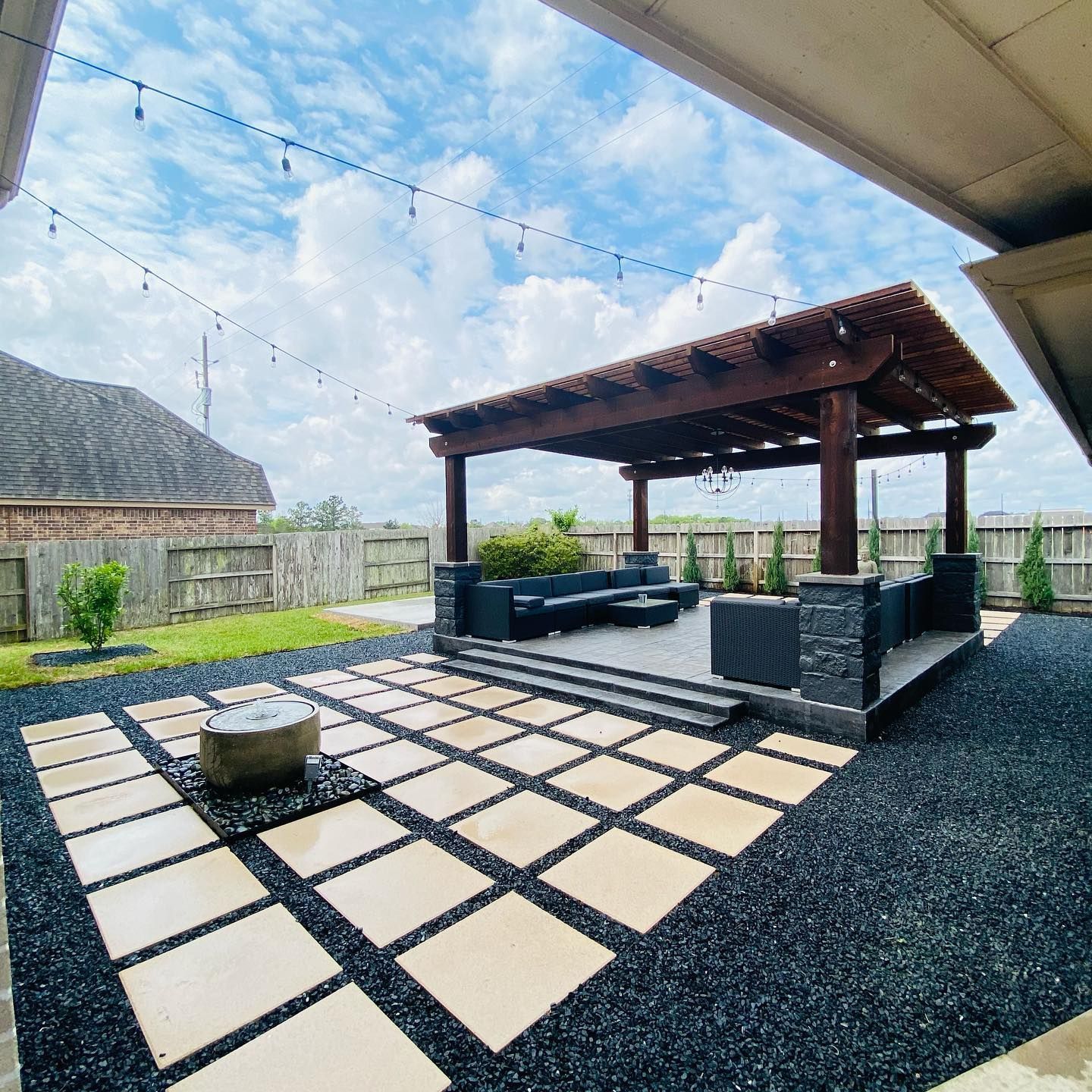 Outdoor patio with pergola, seating, fire pit, and stone pavers on black gravel.
