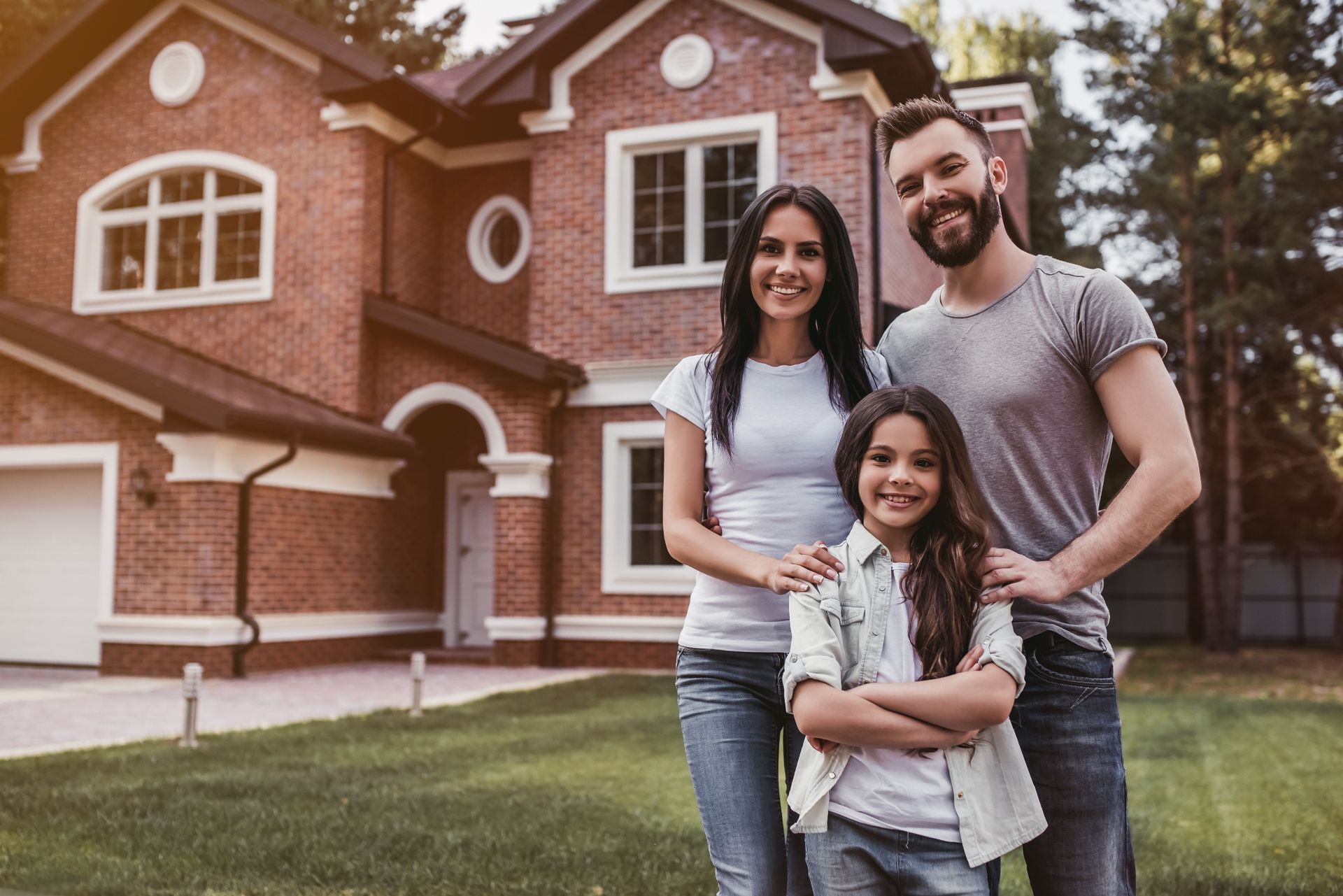 A family stands smiling in front of a brick house on a sunny day.