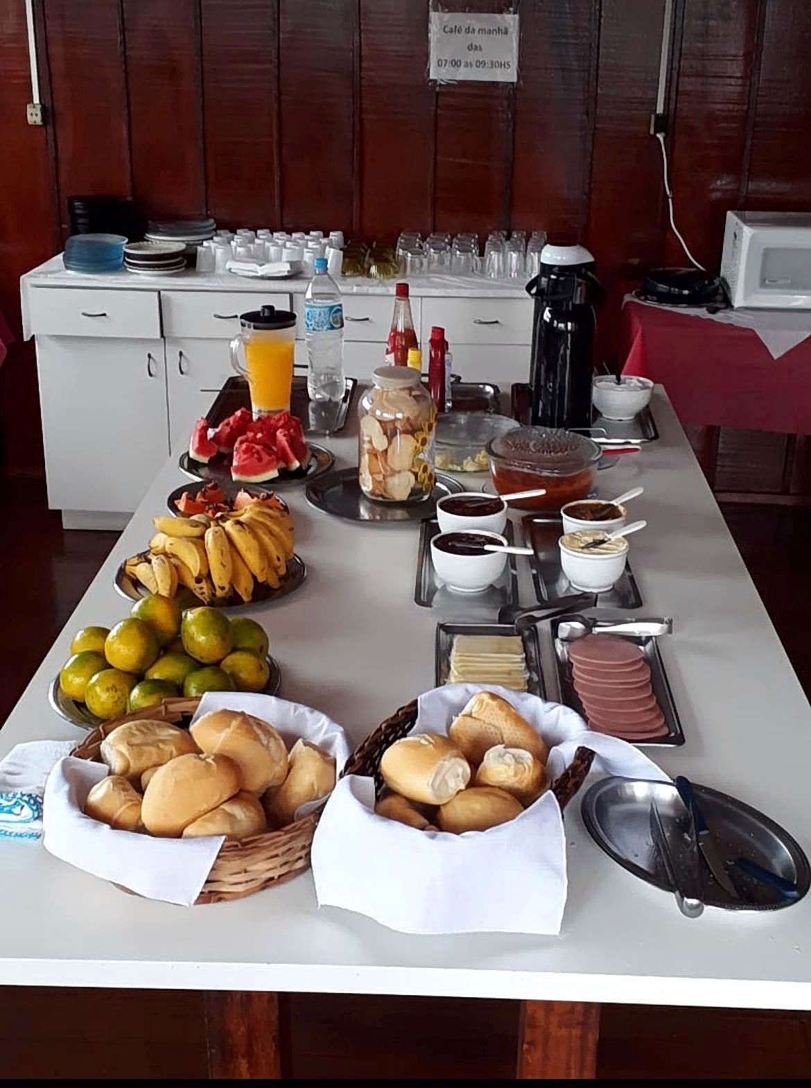 Buffet de café da manhã com bananas, limões, doces, cereais, café e suco em uma mesa.