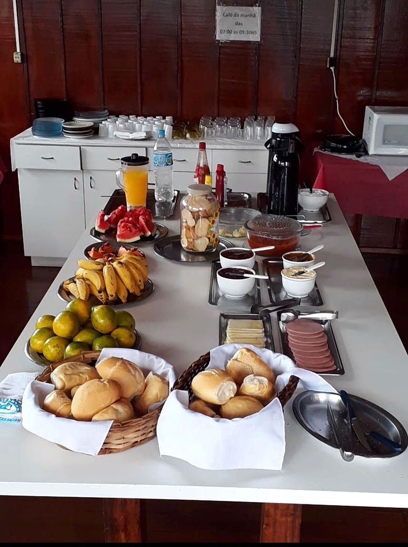 Buffet de café da manhã com bananas, limões, doces, cereais, café e suco em uma mesa.