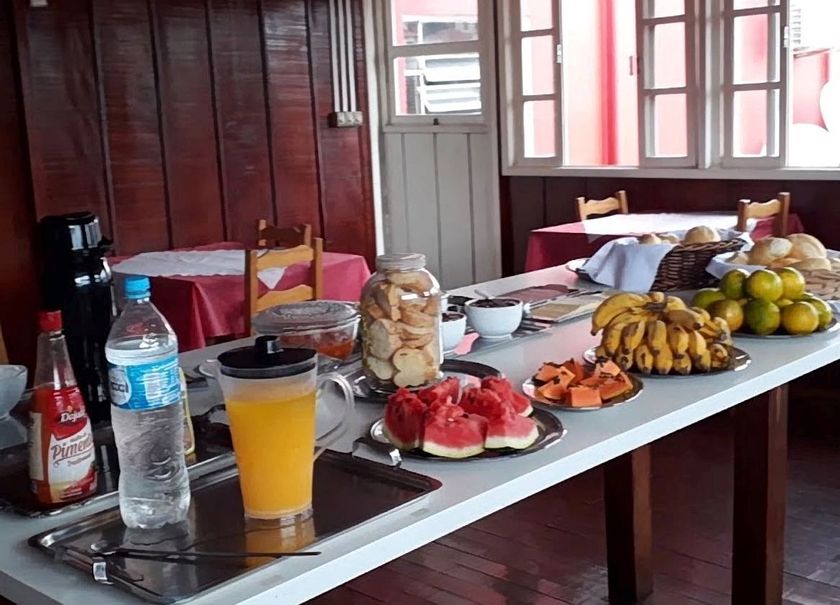 Mesa com frutas, bebidas e petiscos disposta em uma sala de madeira junto a uma janela.
