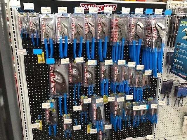 Auto parts store aisle with hanging blue-handled tools and drill bit sets on pegboard displays