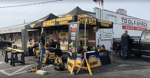 Tool demo booth with black-and-yellow canopy, tools on display, and people in a parking lot.