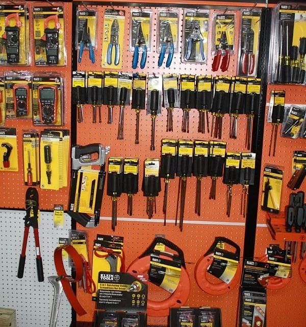 A wall display of hand tools in orange packaging, including pliers, screwdrivers, saws, and measuring tools.