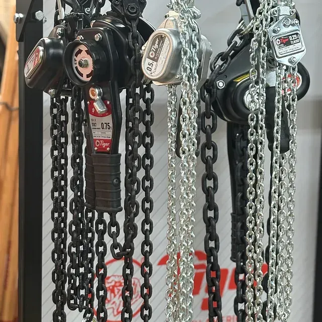 Industrial chain hoists hanging in a row, with black and silver chains in a workshop setting