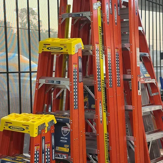 Stacked red extension ladders with yellow tops in a store aisle.