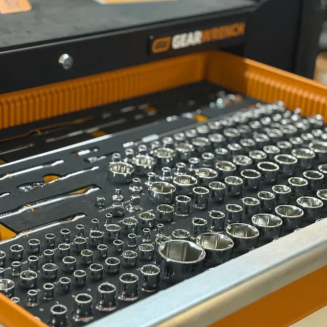 Open socket wrench set in a foam tray, with a black-and-orange tool case in the background