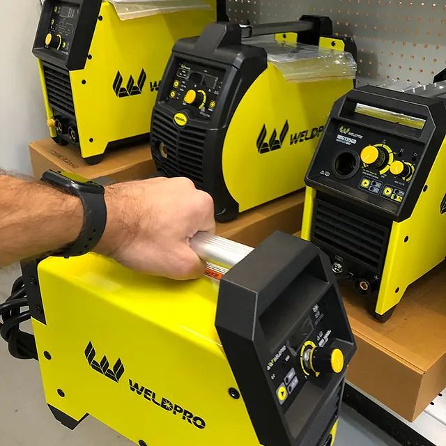 Hand lifting a yellow WELDPRO machine from a shelf with several similar units nearby.