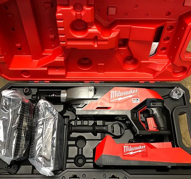 Open red Milwaukee tool case with two wrapped battery packs and a cordless saw inside