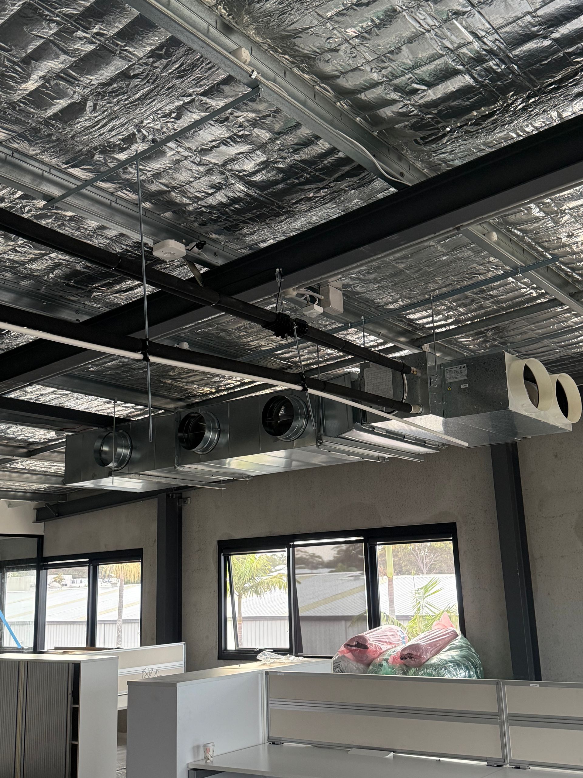 Open office with exposed ceiling, black beams, windows, and white cubicle partitions — Deltech HVACR in Georgetown, NSW