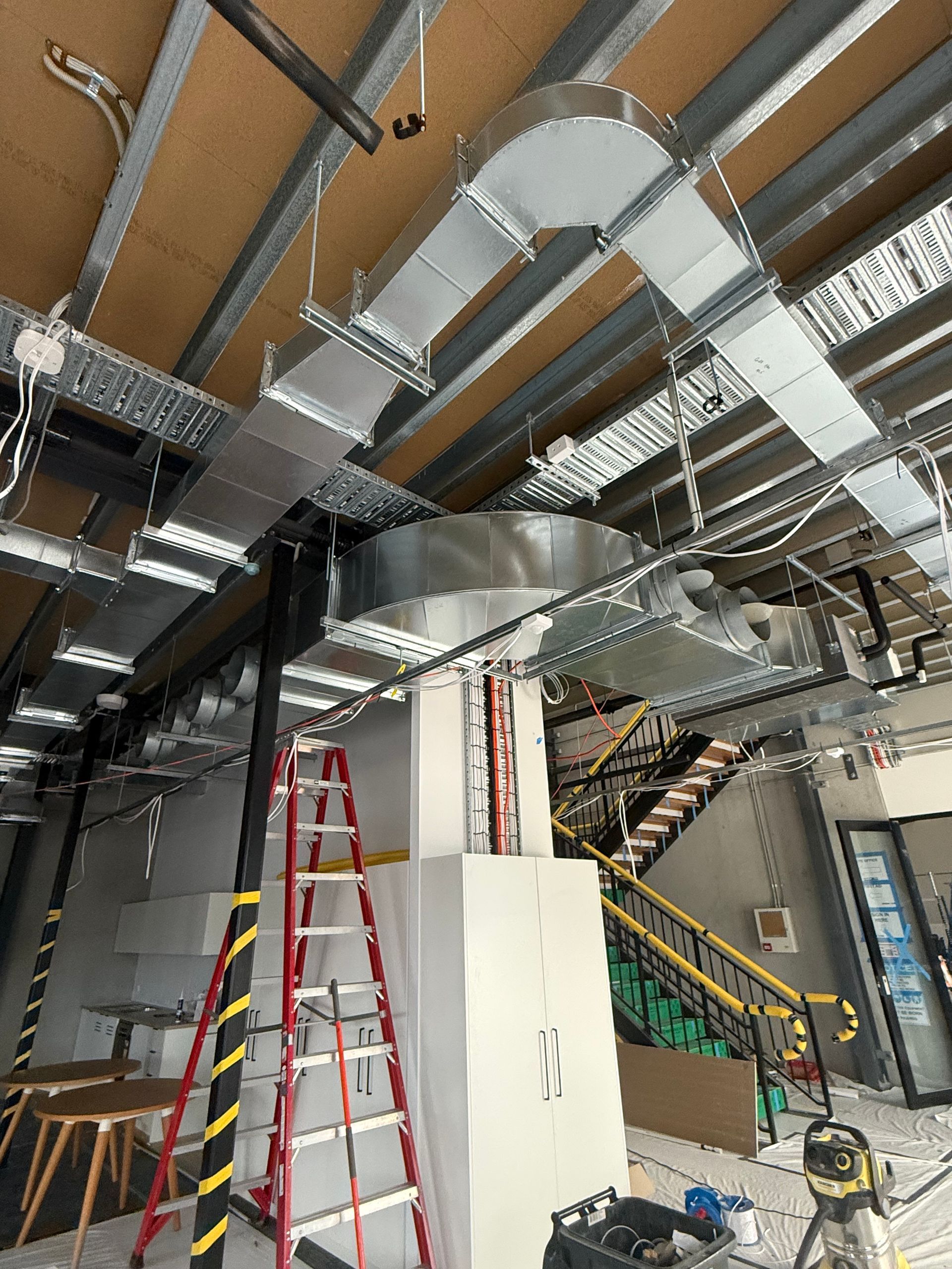 Industrial ceiling with exposed ductwork and pipes; red ladder and equipment in a worksite interior — Deltech HVACR in Georgetown, NSW