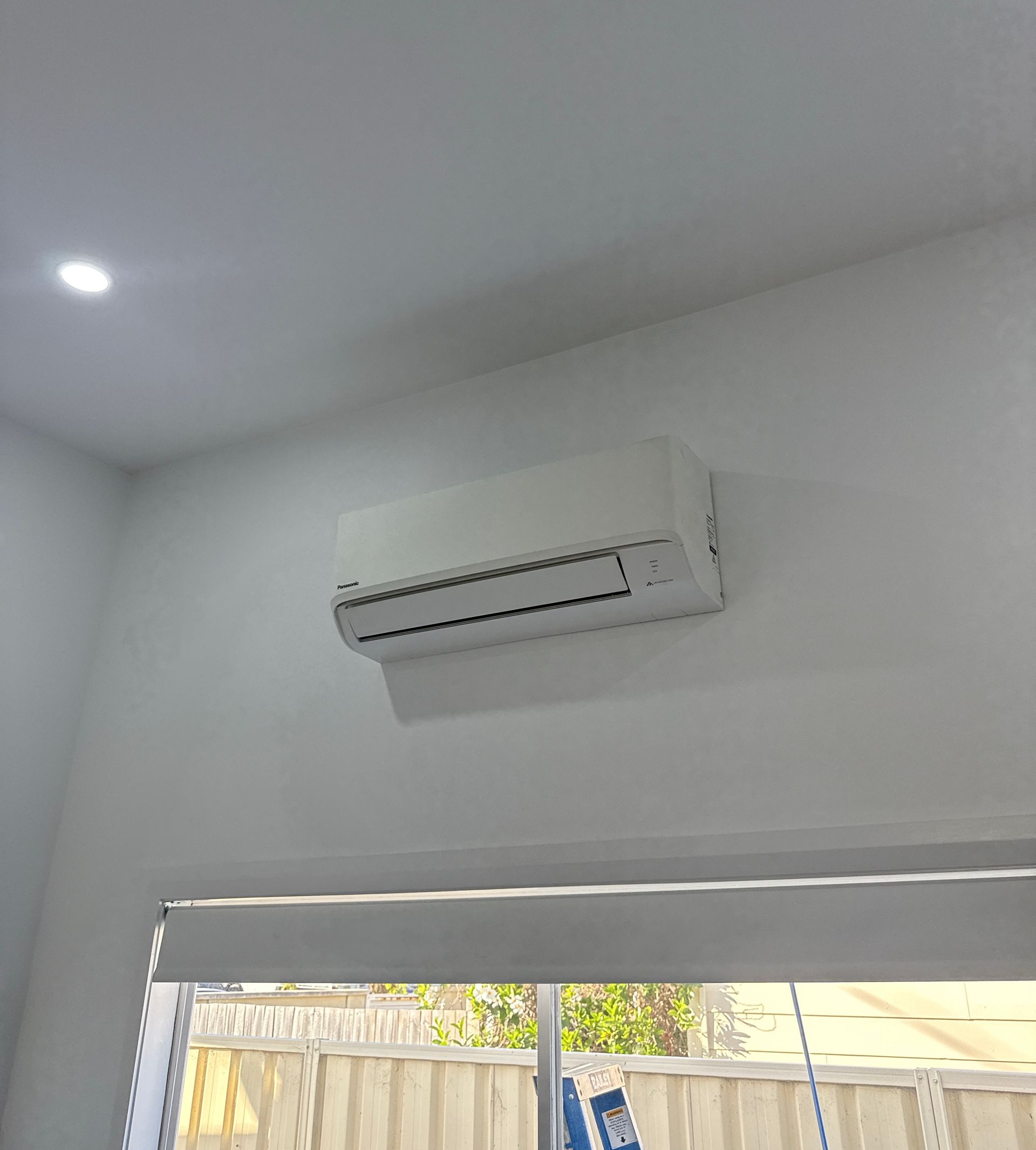 White wall-mounted air conditioner above a window in a bright room — Deltech HVACR in Georgetown, NSW